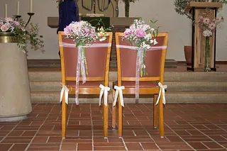 Geschmückte Stühle mit Blumen in einer Kirche, zum Altar ausgerichtet.