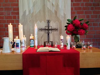 Geschmückter Tisch mit Kerzen, Kreuz, Bibel und roten Blumen.